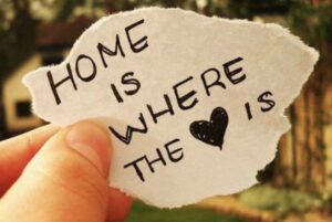 An image of a hand holding a torn piece of paper, with handwritten "home is where the [heart] is". Instead of the word "heart" is a coloured in image of a heart.
