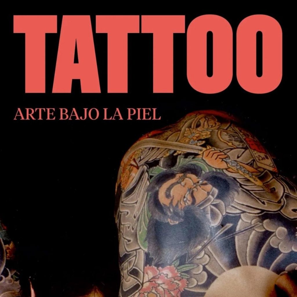 Thick bold capital letters read 'TATTOO' in red, with 'ARTE BAJO LA PIEL' in smaller font underneath. The background of the image is black, with a densely traditionally tattooed back taking up the bottom right half of the image. The back tattoo is east Asian imagery of a man holding a sword, with a large sun and its rays and some clouds done in black and grey shading.
