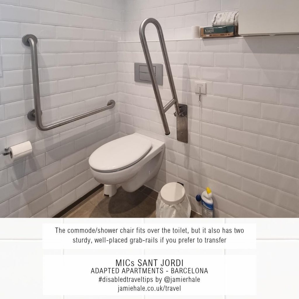Superimposed on top of a picture of a white toilet in a corner, with wall mounted grab rails on one side, and a drop-down grab rail on the other. It has a bin beside it, a flush above it, and a shelf and cupboard above it is the text "MICs Sant Jordi, adapted apartments, Barcelona, the commode or shower chat fits over the toilet, but it also has two sturdy well placed grab rails if you prefer to transfer, #DisabledTravelTips by @jamierhale jamiehale.co.uk/travel"